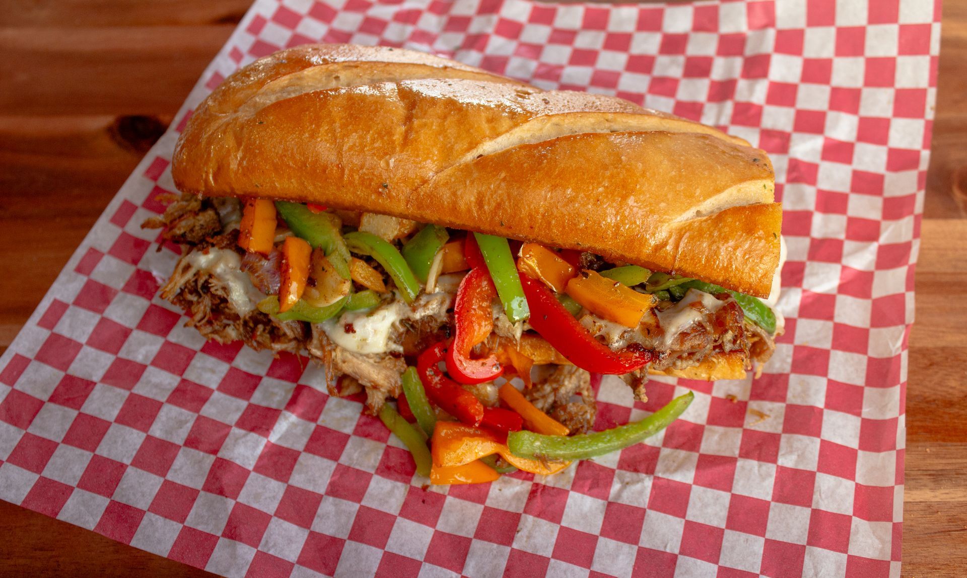 Philly cheesesteak sandwich with peppers and onions on a red checkered paper.