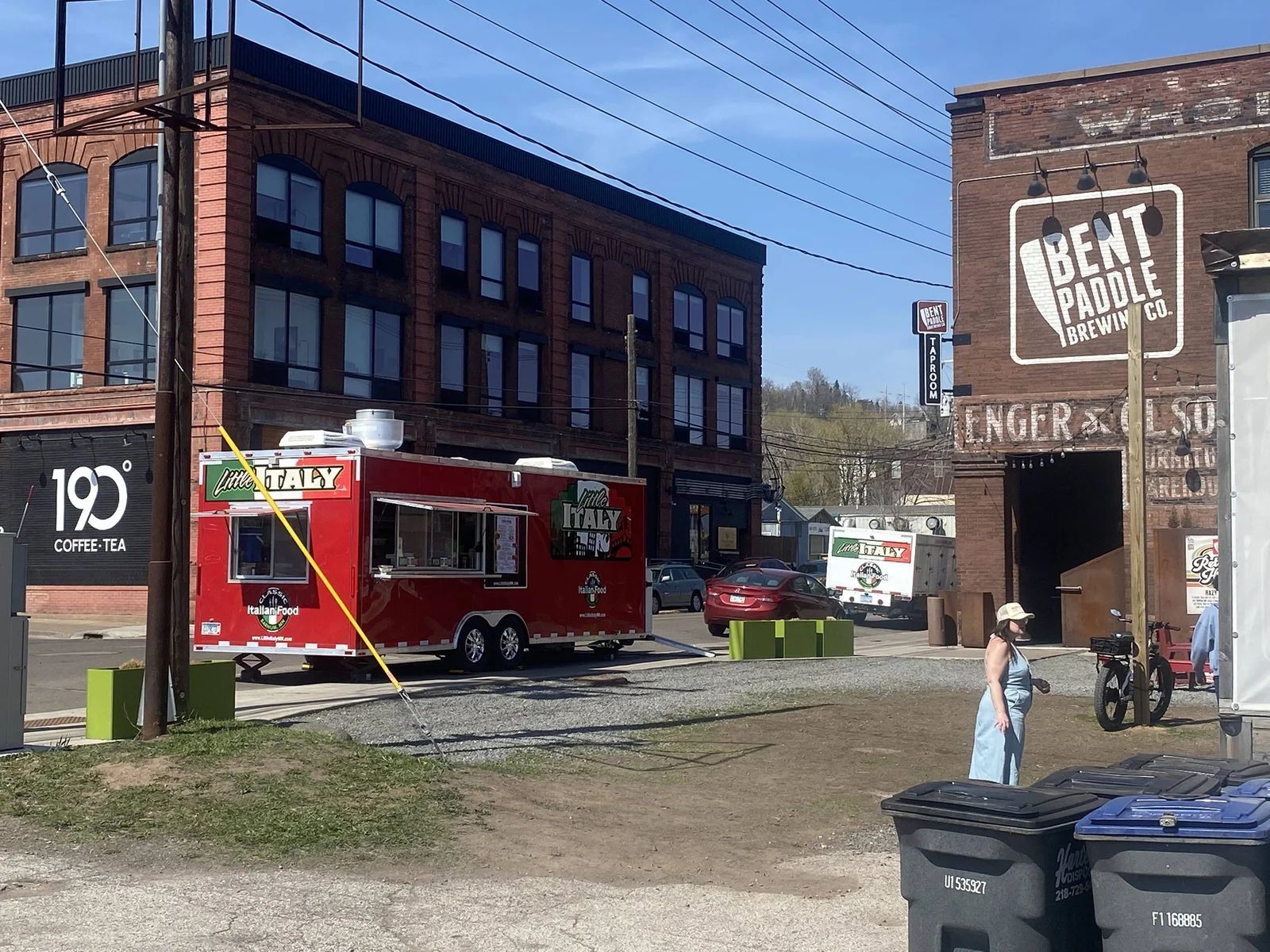 Red food truck parked in front of brick buildings, a person stands near trash cans.
