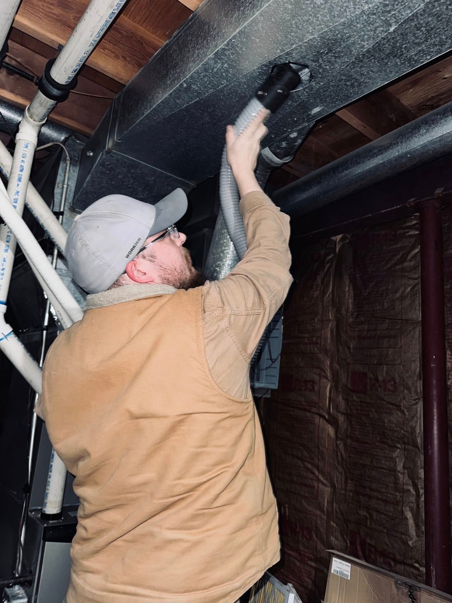 A man is using a vacuum cleaner to clean a duct in a basement.