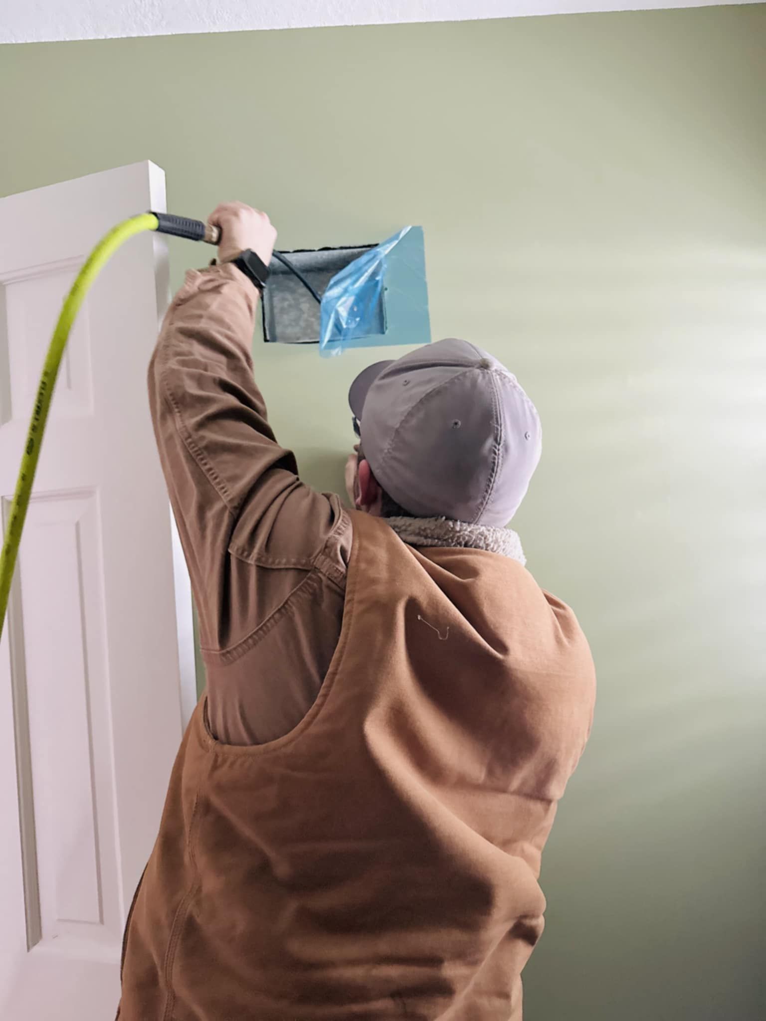 A man is measuring a hole in a wall with a tape measure.