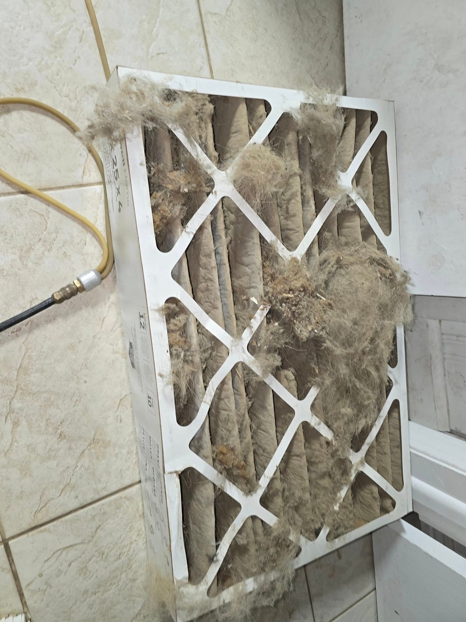 A dirty air filter is sitting on the floor next to a hose.