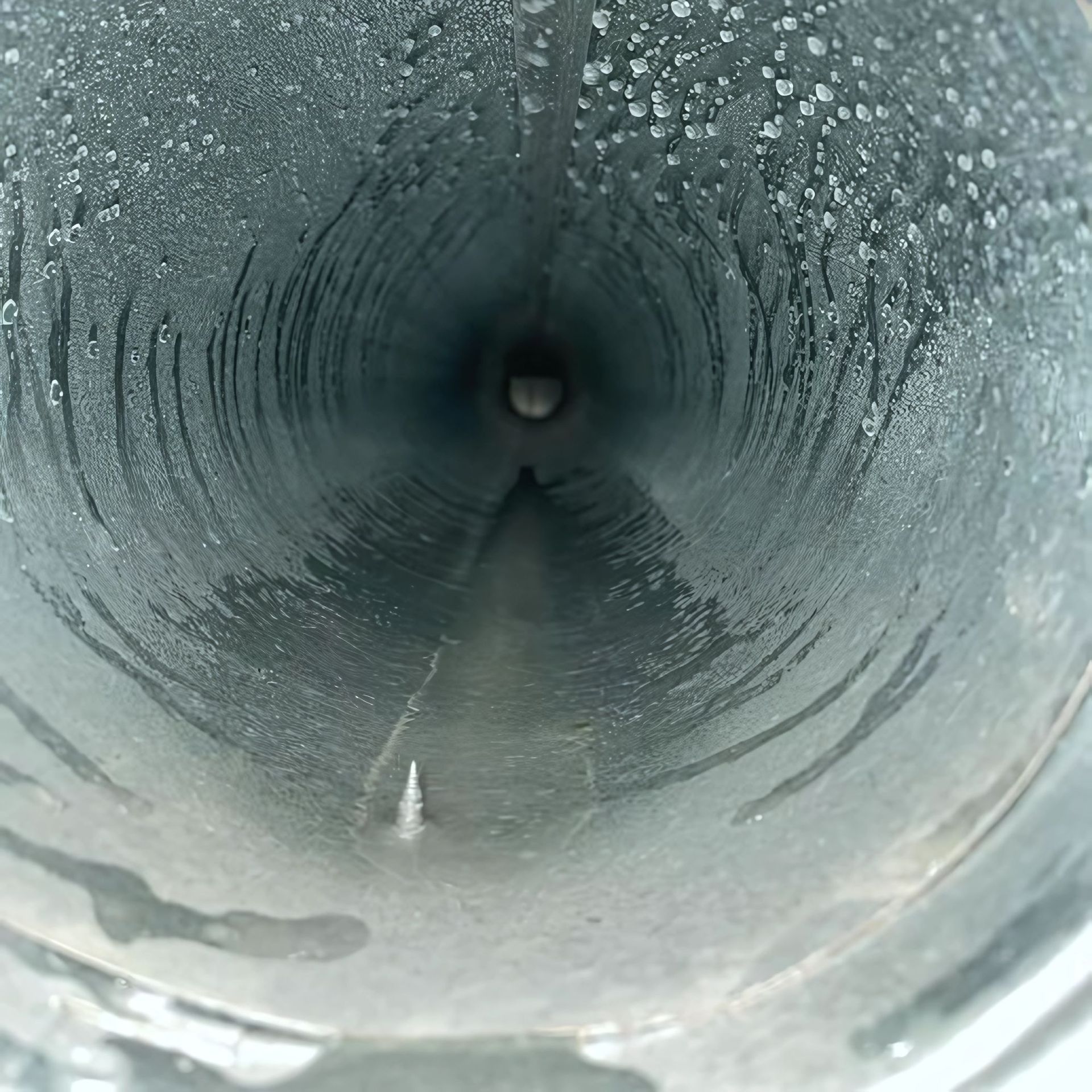 Duct Wrangler, LLC - Looking down inside a wet, metallic pipe. Condensation and streaks of water are visible.