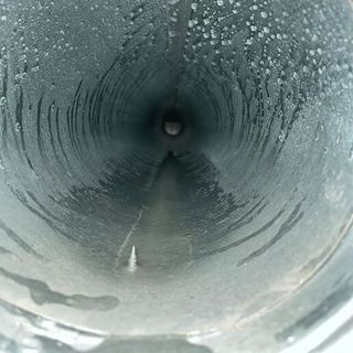 Duct Wrangler, LLC - An aerial view of a man on a ladder cleaning a gutter on the side of a house.