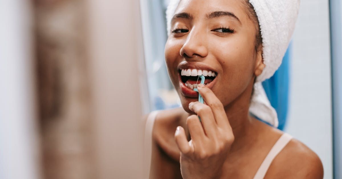 A woman with a towel wrapped around her head is brushing her teeth in front of a mirror.