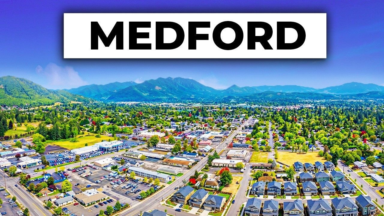 Aerial view of Medford with city buildings, neighborhoods, and mountains in the distance.