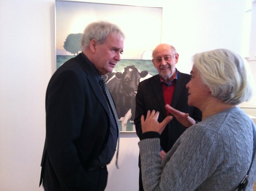 Zwei Männer und eine Frau unterhalten sich vor einem Gemälde von Kühen