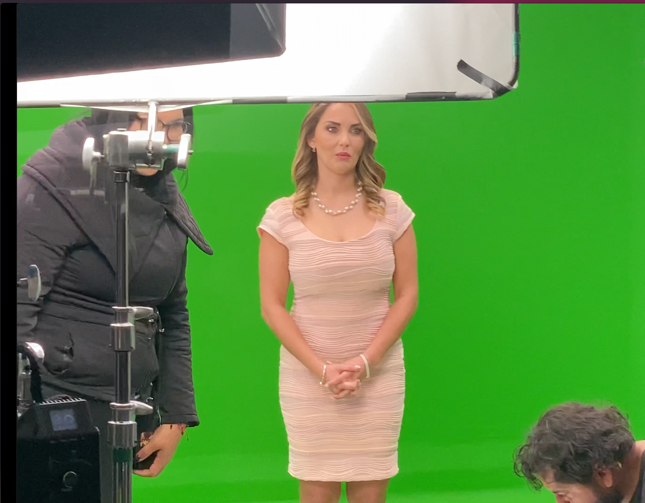 Una mujer con un vestido rosa está parada frente a una pantalla verde.