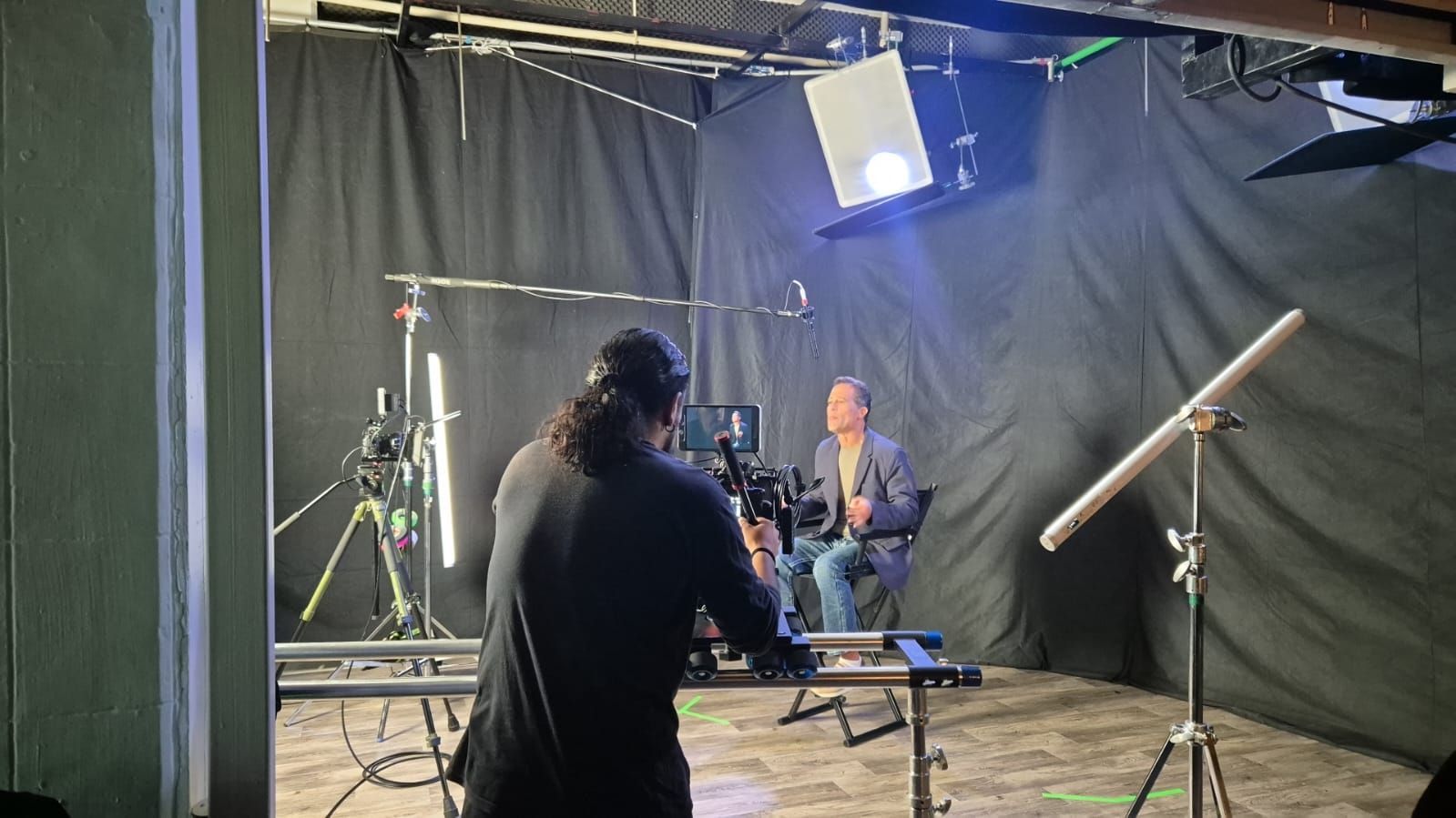 Un hombre está sentado en una silla frente a una cámara en un estudio.