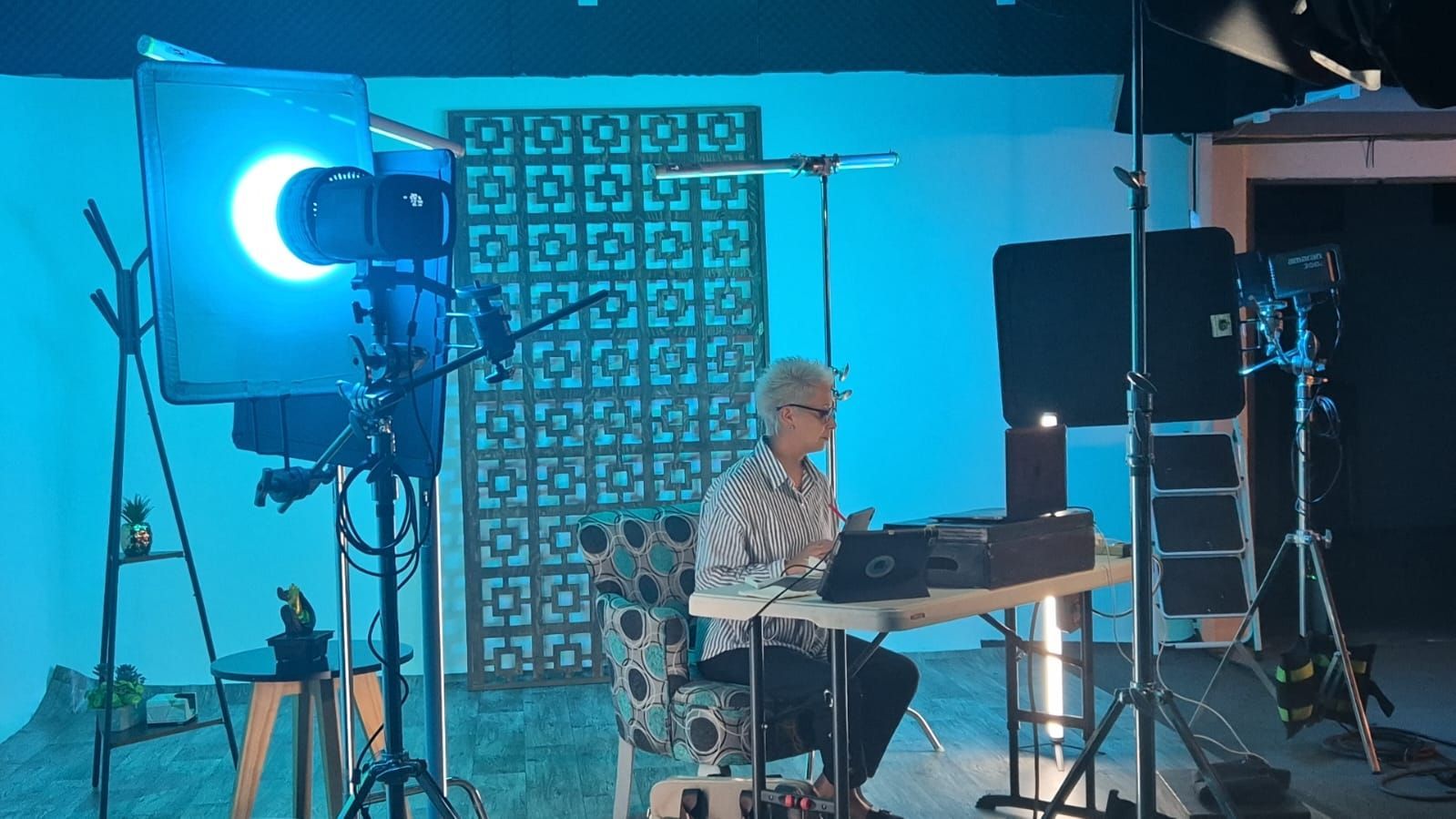 Una mujer está sentada en una mesa frente a una pared azul en un estudio.