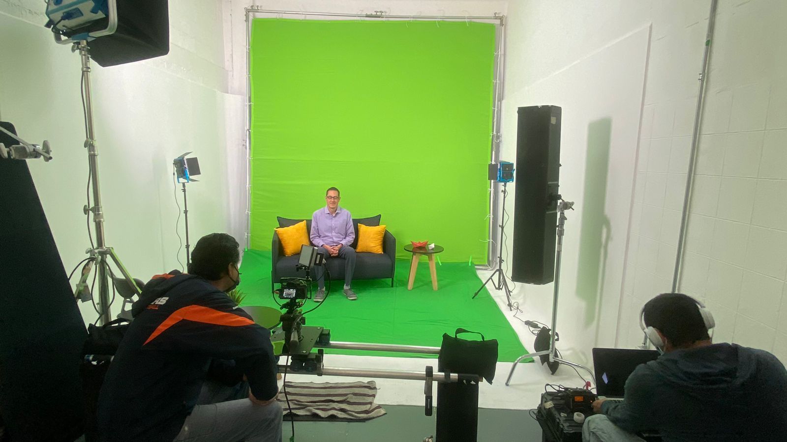Un hombre está sentado en un sofá frente a una pantalla verde en un estudio.
