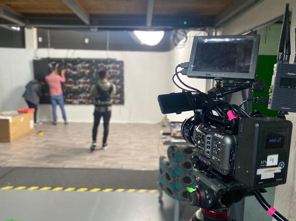 Una cámara está sobre una mesa en una habitación con gente de pie en el fondo.