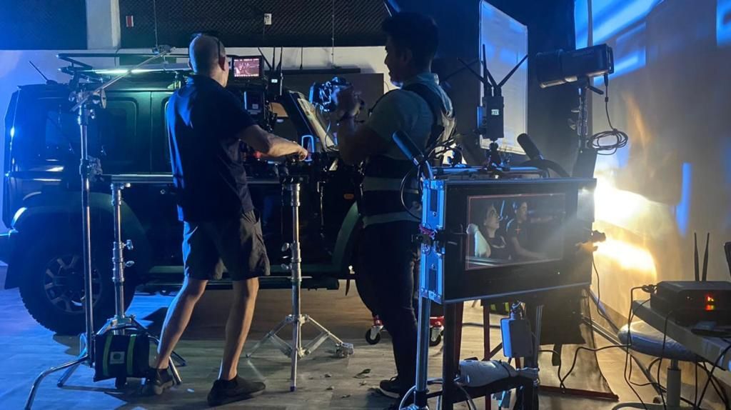 Dos hombres están parados frente a una cámara en una habitación oscura.