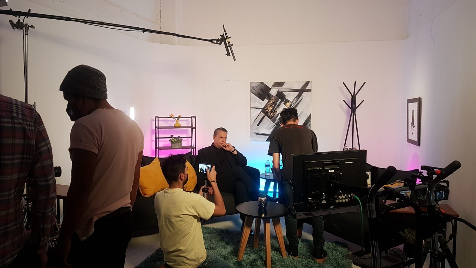 Un grupo de personas está de pie en una habitación tomando fotografías de un hombre sentado en un sofá.