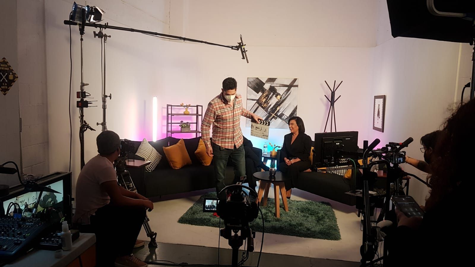 Un hombre y una mujer están sentados en un sofá en una sala de estar frente a una cámara.