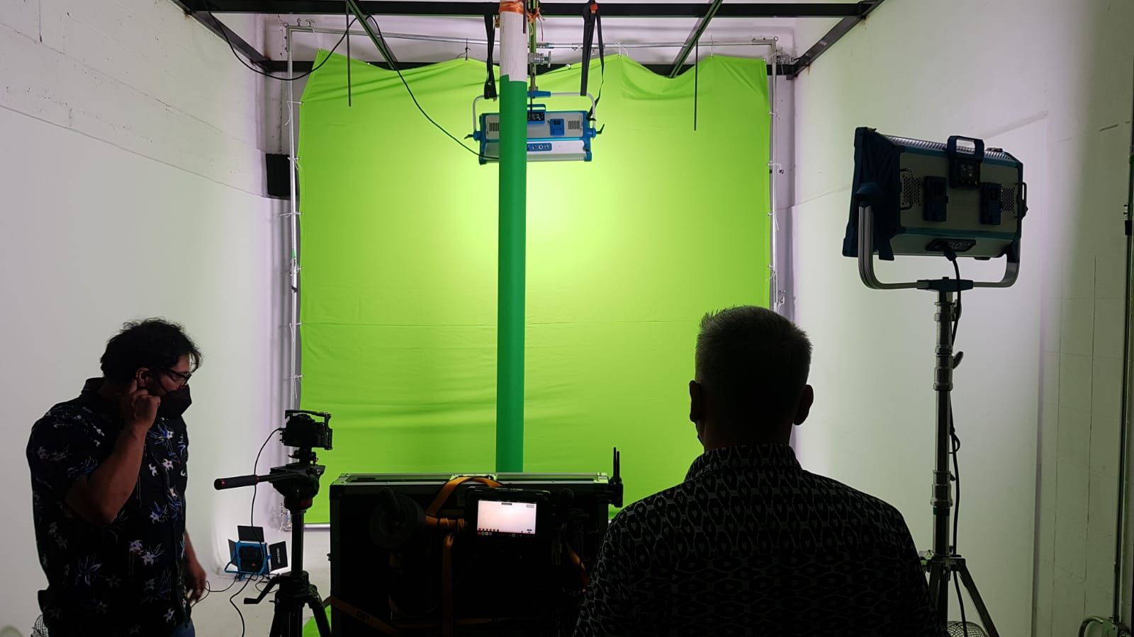 Dos hombres están parados frente a una pantalla verde en un estudio.