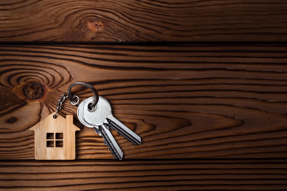 Keys and House-shaped Keychain Resting on a Wooden Surface — Property Transfer Professionals In Erina, NSW