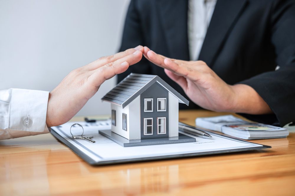 Hands Protect a Miniature House on a Desk With Documents and Money — Property Transfer Professionals In Erina, NSW