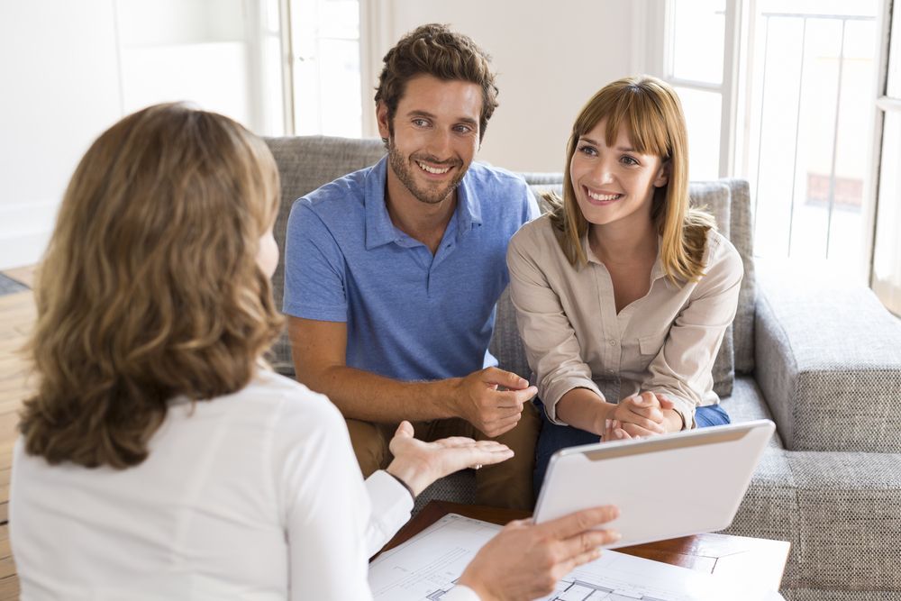Real Estate Agent Reviewing Plans With a Smiling Couple on a Couch — Property Transfer Professionals In Wyee, NSW