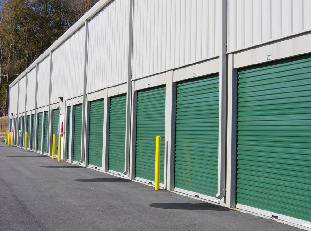 Row of Green Storage Unit Doors on a White Building, Asphalt Driveway — Property Transfer Professionals In Bateau Bay, NSW