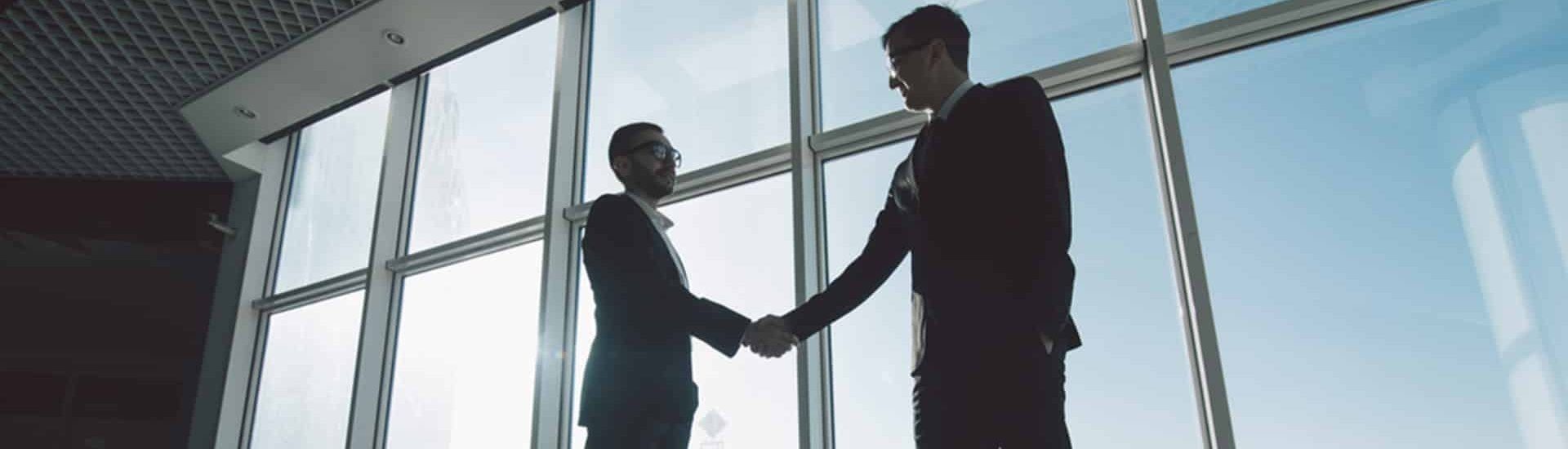 Two Men in Suits Shaking Hands in Front of a Large Window — Property Transfer Professionals In Wyong, NSW