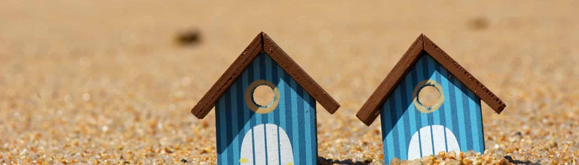 Two Blue Birdhouses With Brown Roofs Sit on a Sandy Beach — Property Transfer Professionals In Wyong, NSW