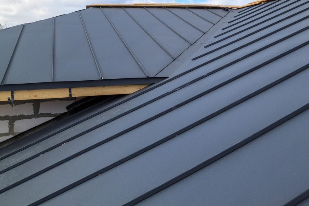 Grey folding roof being installed on a house under construction, resting on a waterproofing layer.