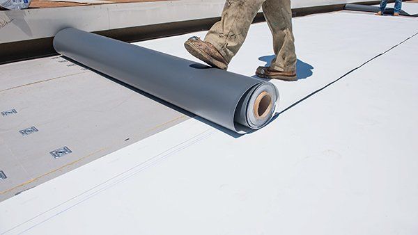 An experienced roofer carefully installing TPO roofing sheets onto a commercial building. oofing system being installed.