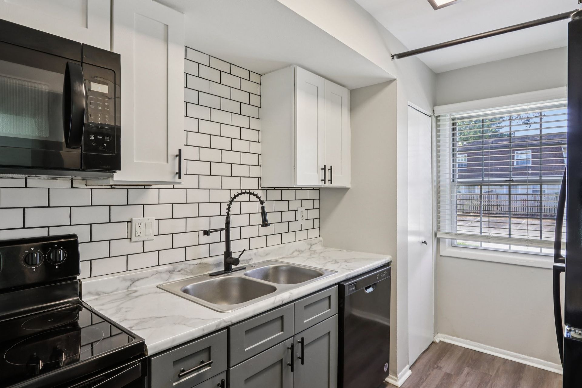 Kitchen with gray and white cabinets, subway tile backsplash, and black appliances.