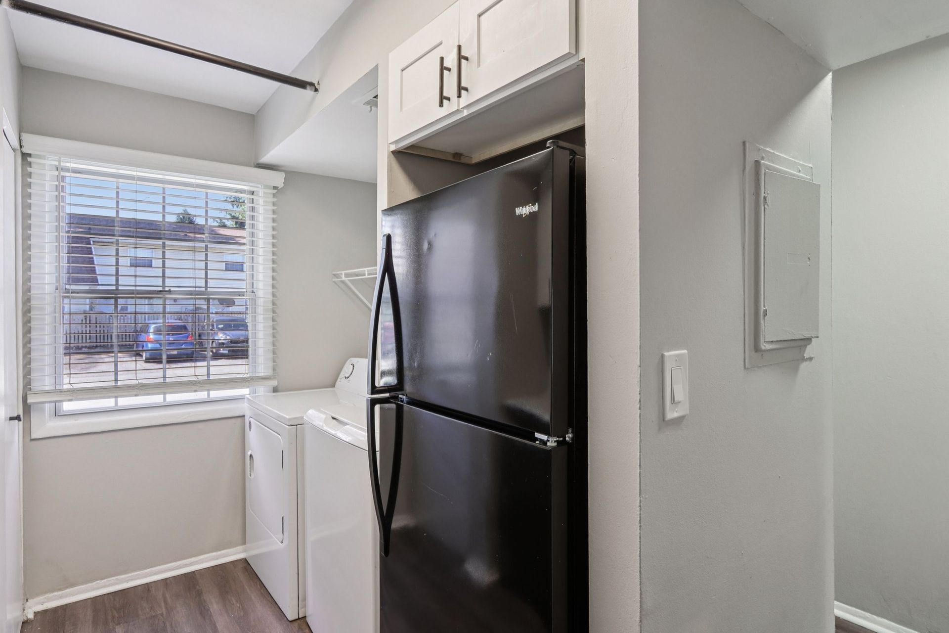 Laundry room with black refrigerator, washer, dryer, and window. Light gray walls and cabinets.
