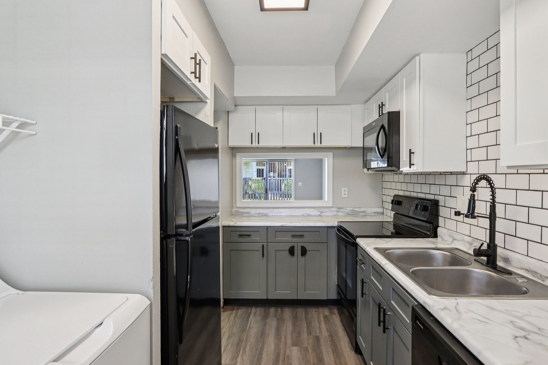 A modern kitchen with white and gray cabinets, black appliances, and a subway tile backsplash.