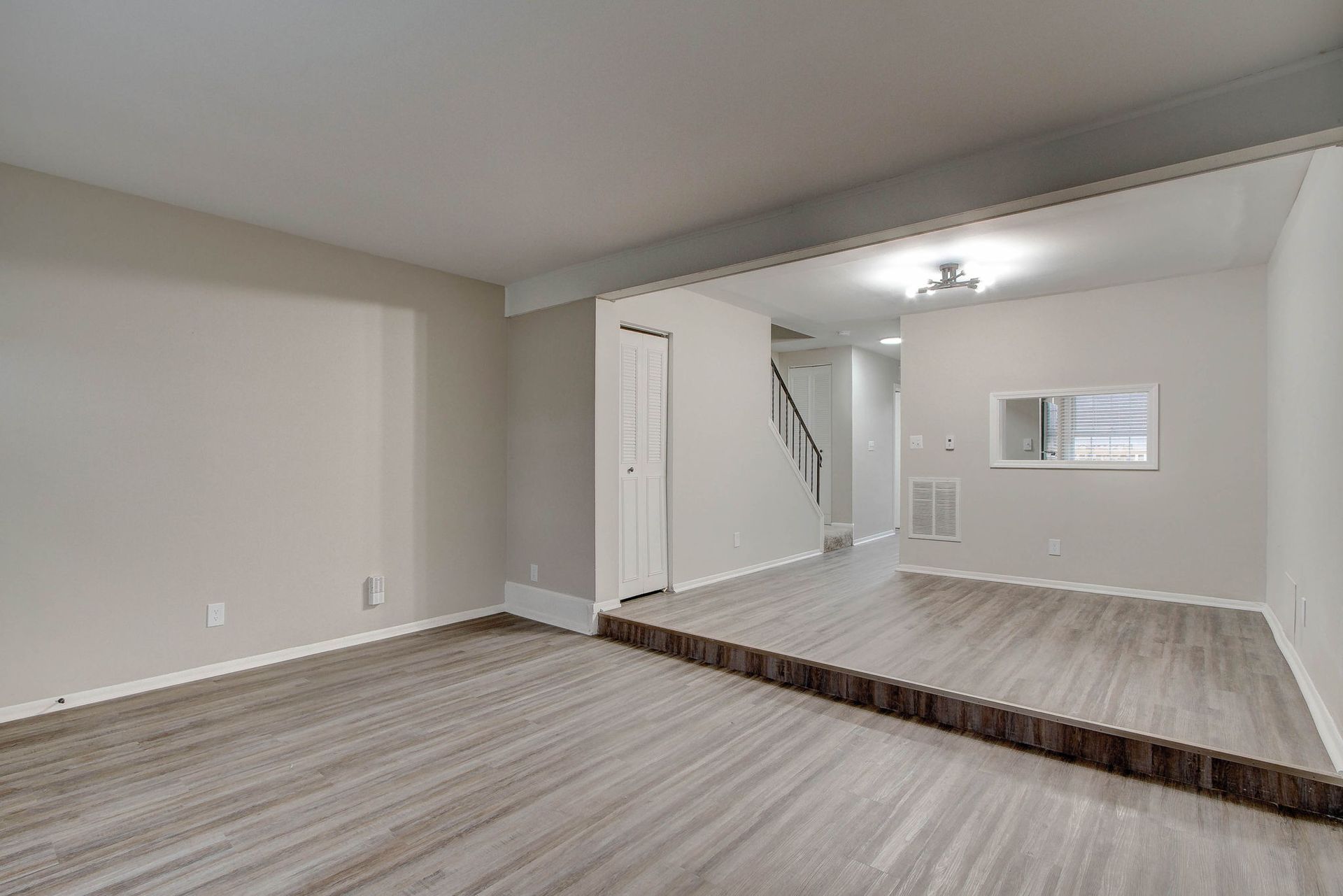 Empty living room with raised floor and stairs in background, neutral color palette.