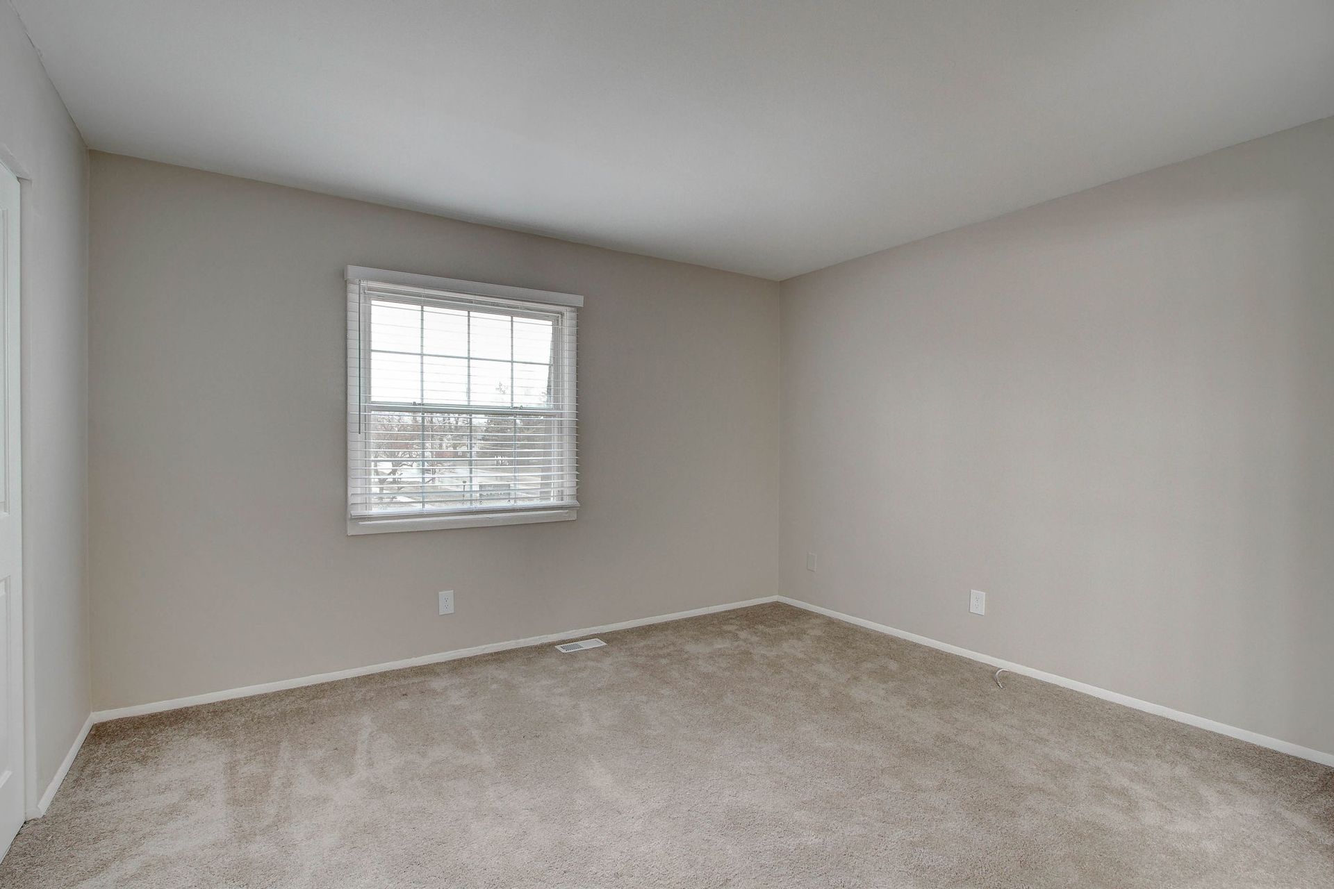Empty room with neutral carpet and walls, a window with a blind, and a doorframe.