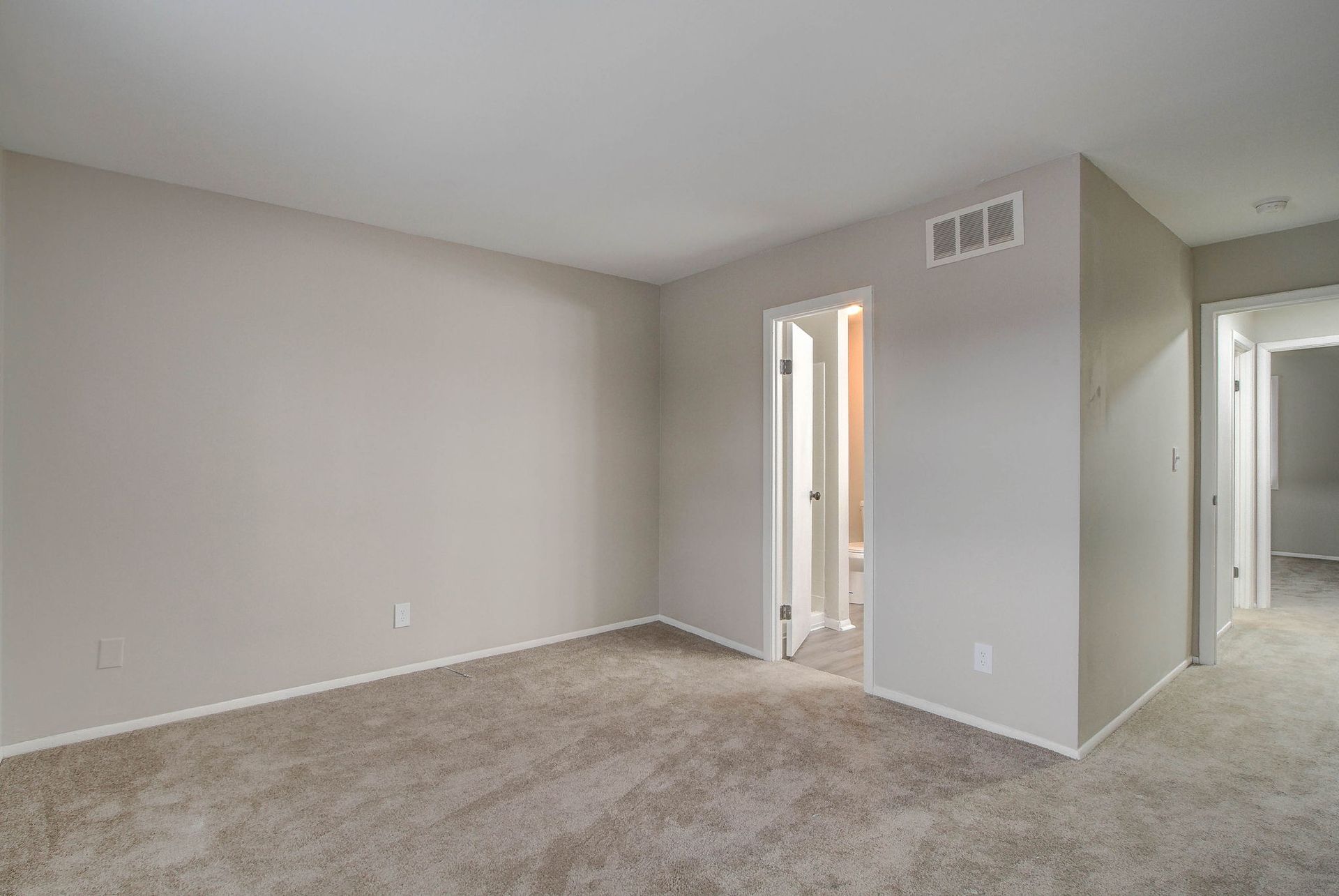 Empty room with beige walls, carpet, and two doorways.