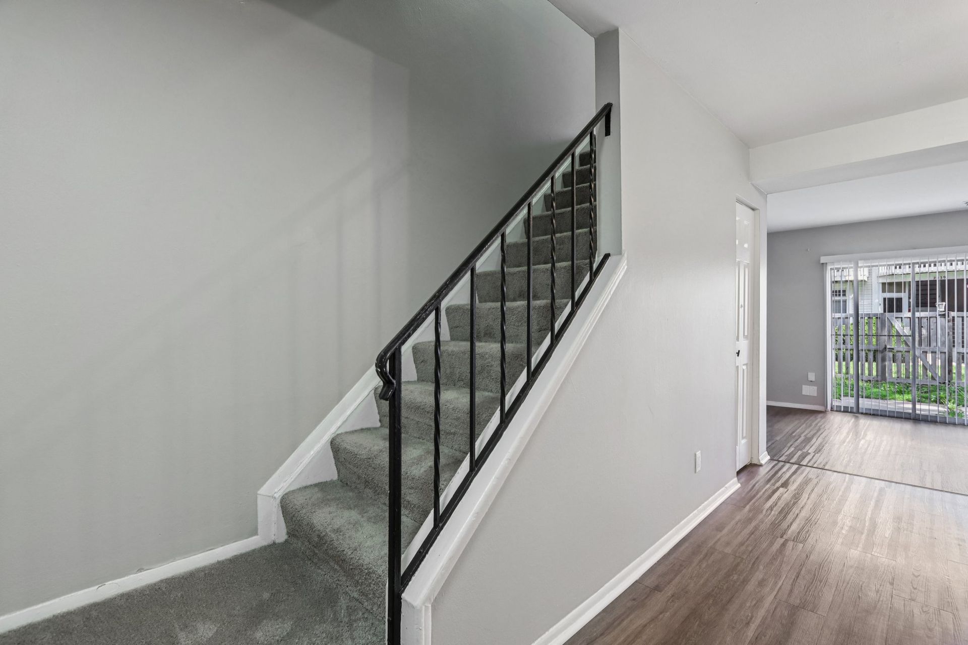 Staircase with black railing, gray carpet, leading up, light gray walls, and a doorway.