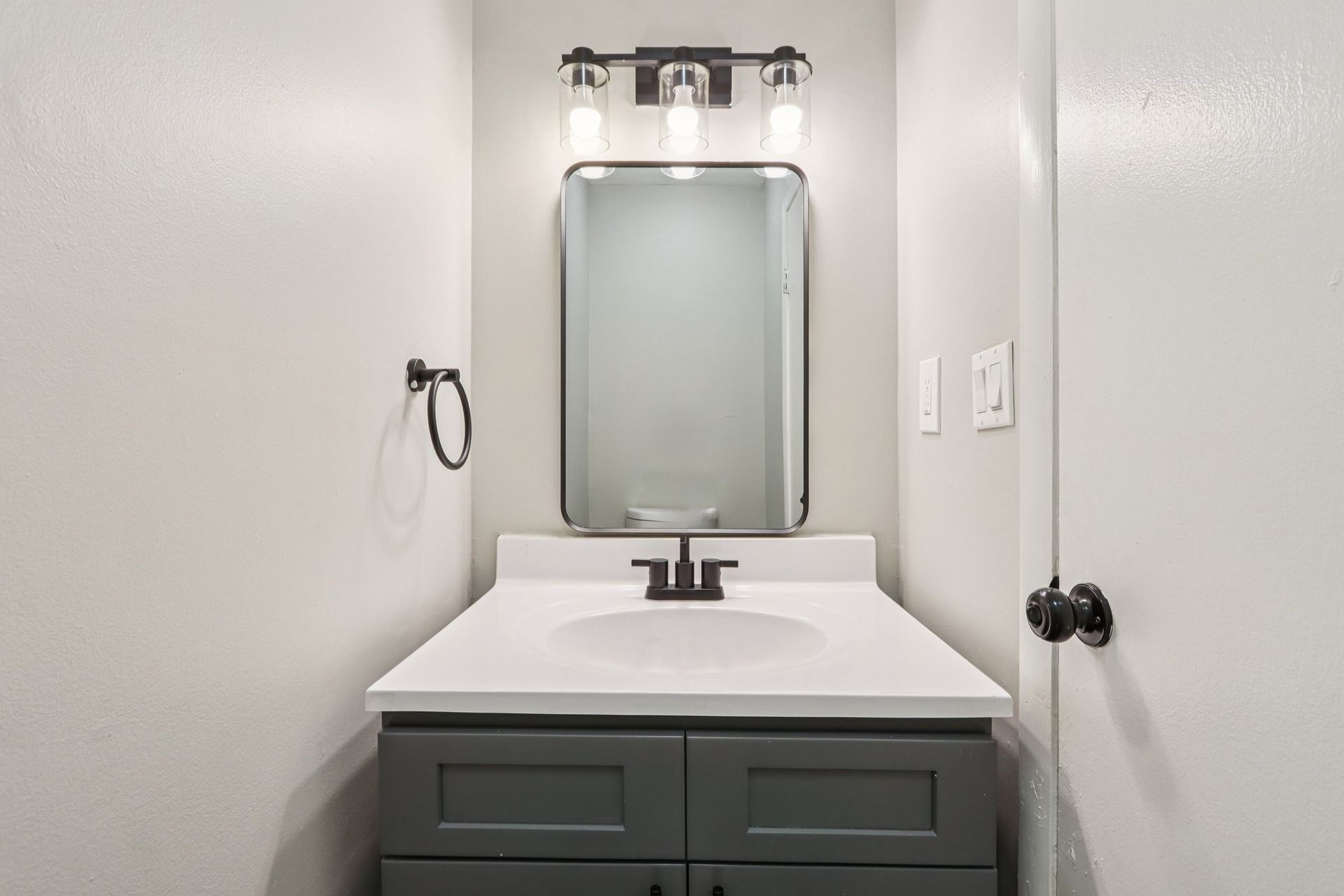 Bathroom with gray vanity, white countertop, black faucet, mirror, and overhead lighting.