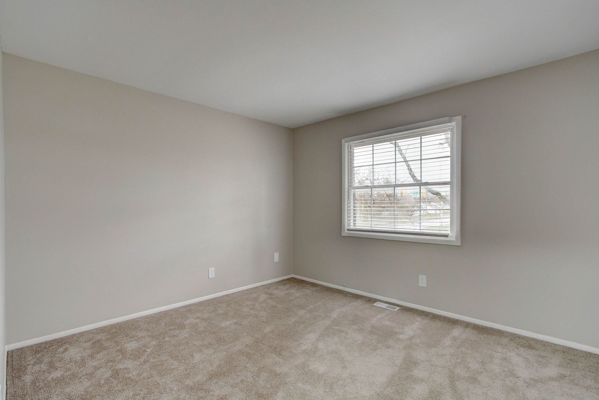 Empty bedroom with beige carpet, light gray walls, and a window.