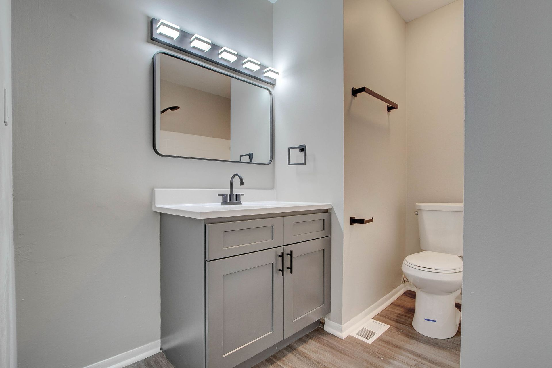 Bathroom with gray vanity, toilet, mirror, and light fixture.