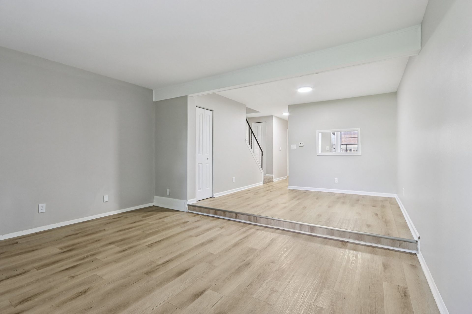Empty living room with light wood floors, light gray walls, and a raised floor section.