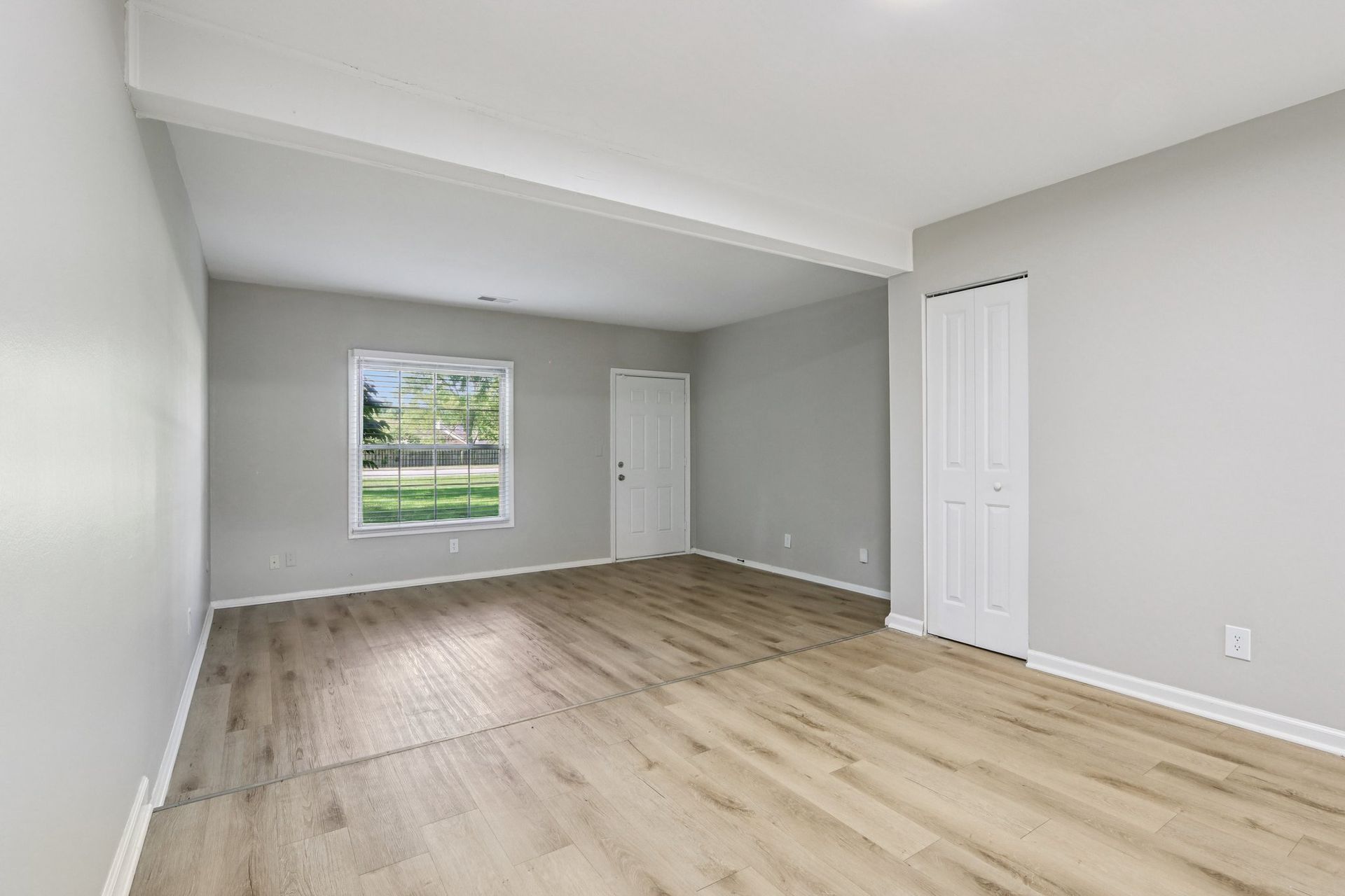 Empty room with light gray walls, light wood floor, a window, and a closet.