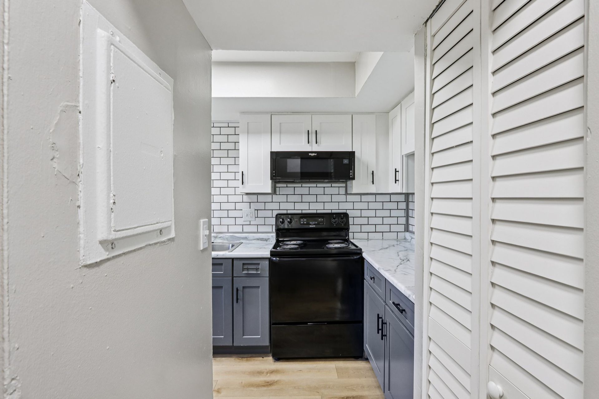 A small, renovated kitchen with white and blue cabinets, black appliances, and a white tiled backsplash.