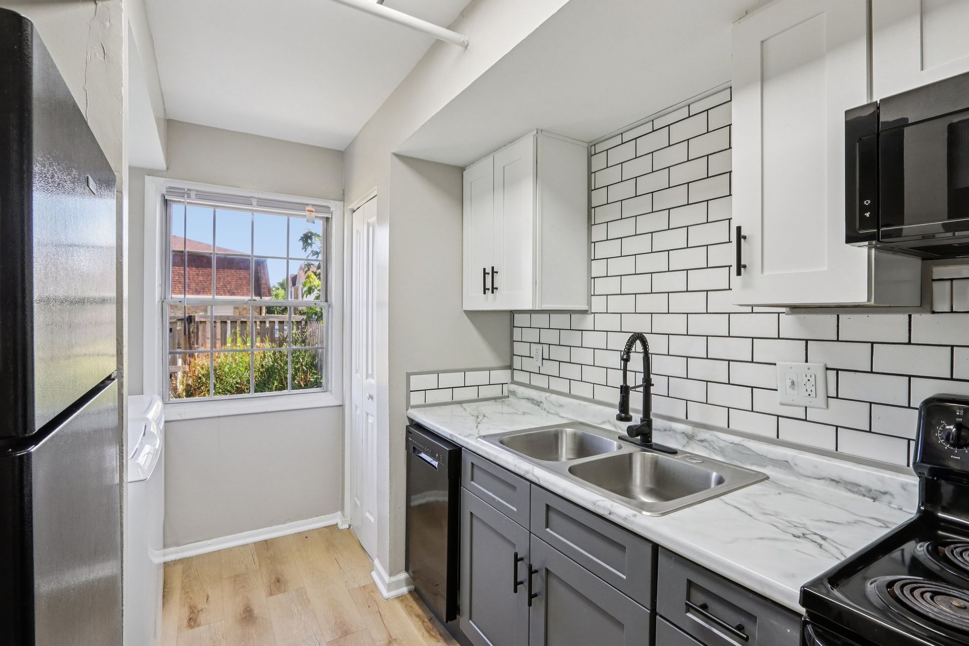 Kitchen with gray and white cabinets, stainless steel sink, white brick backsplash, and wood flooring.