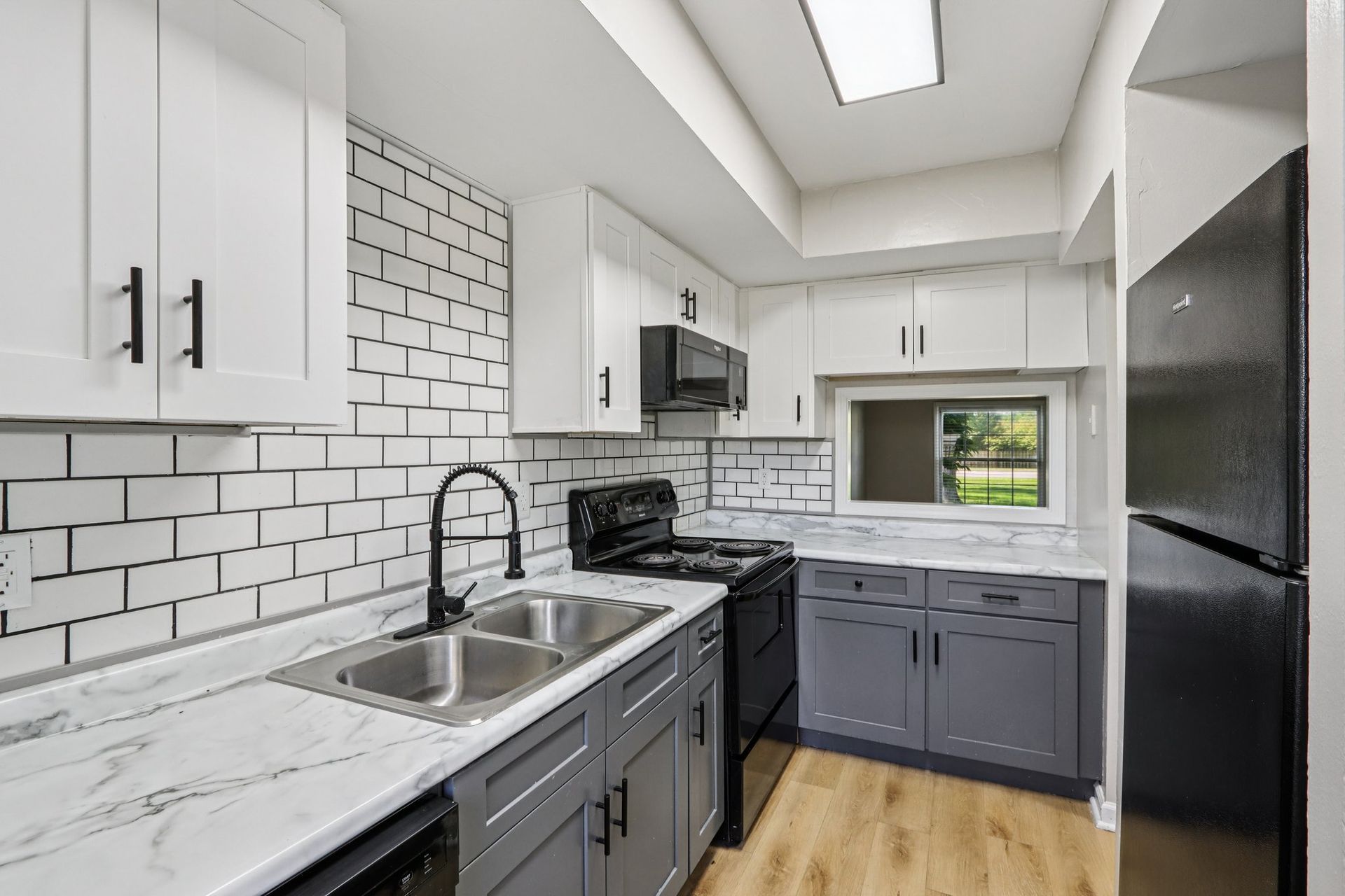 Modern kitchen with white cabinets, grey lower cabinets, and black appliances.