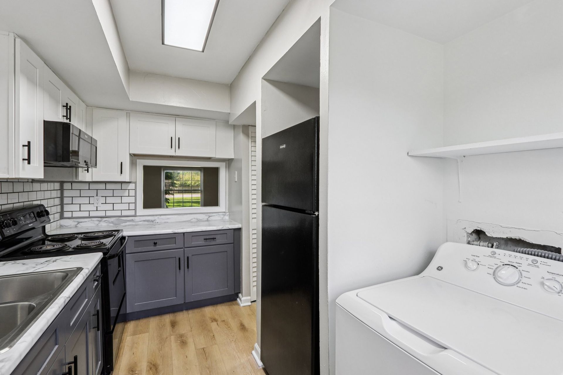 Kitchen with white cabinets, gray lower cabinets, a black refrigerator, and a washing machine.