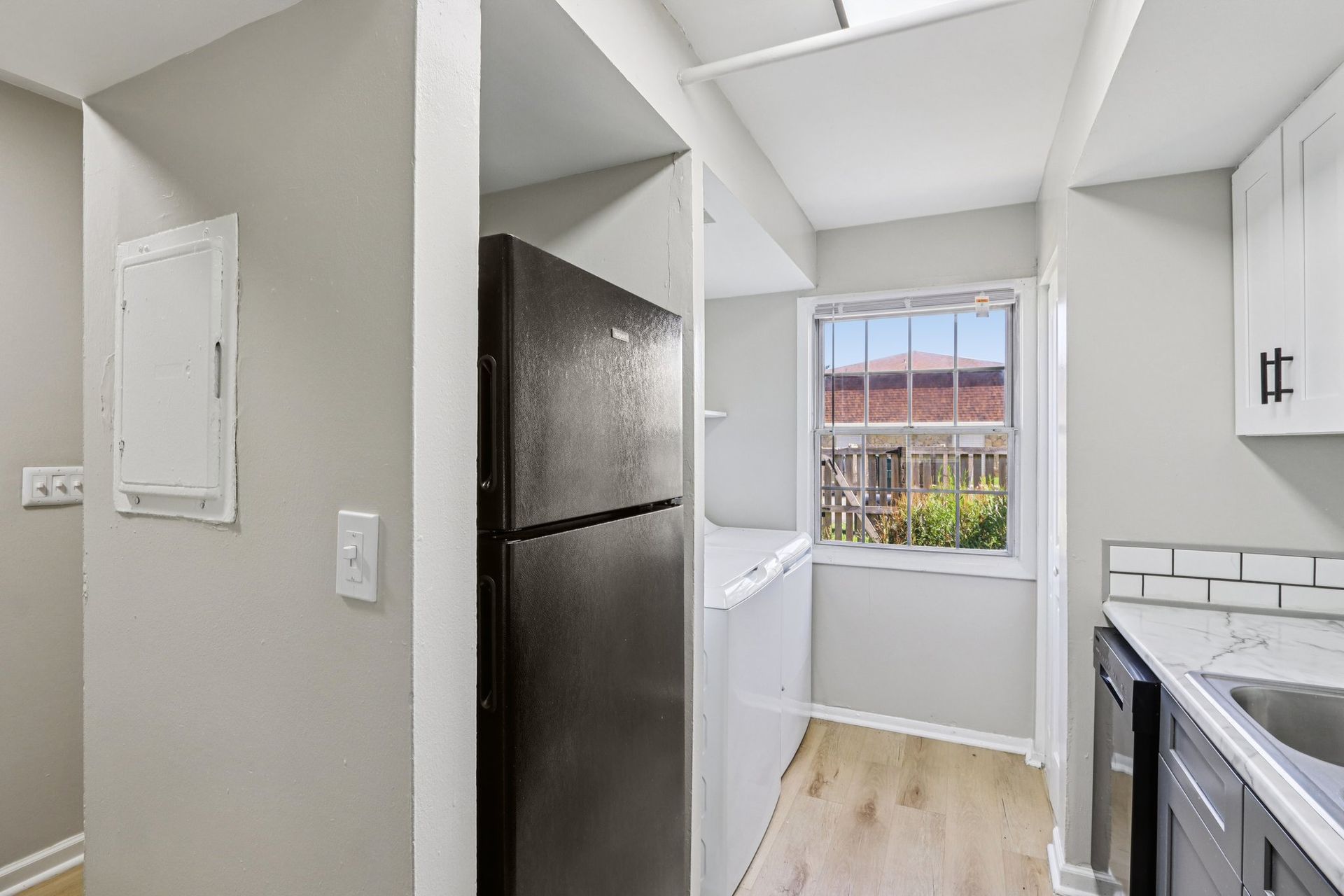 Small kitchen with black fridge, white cabinets, window, and light wood floors.