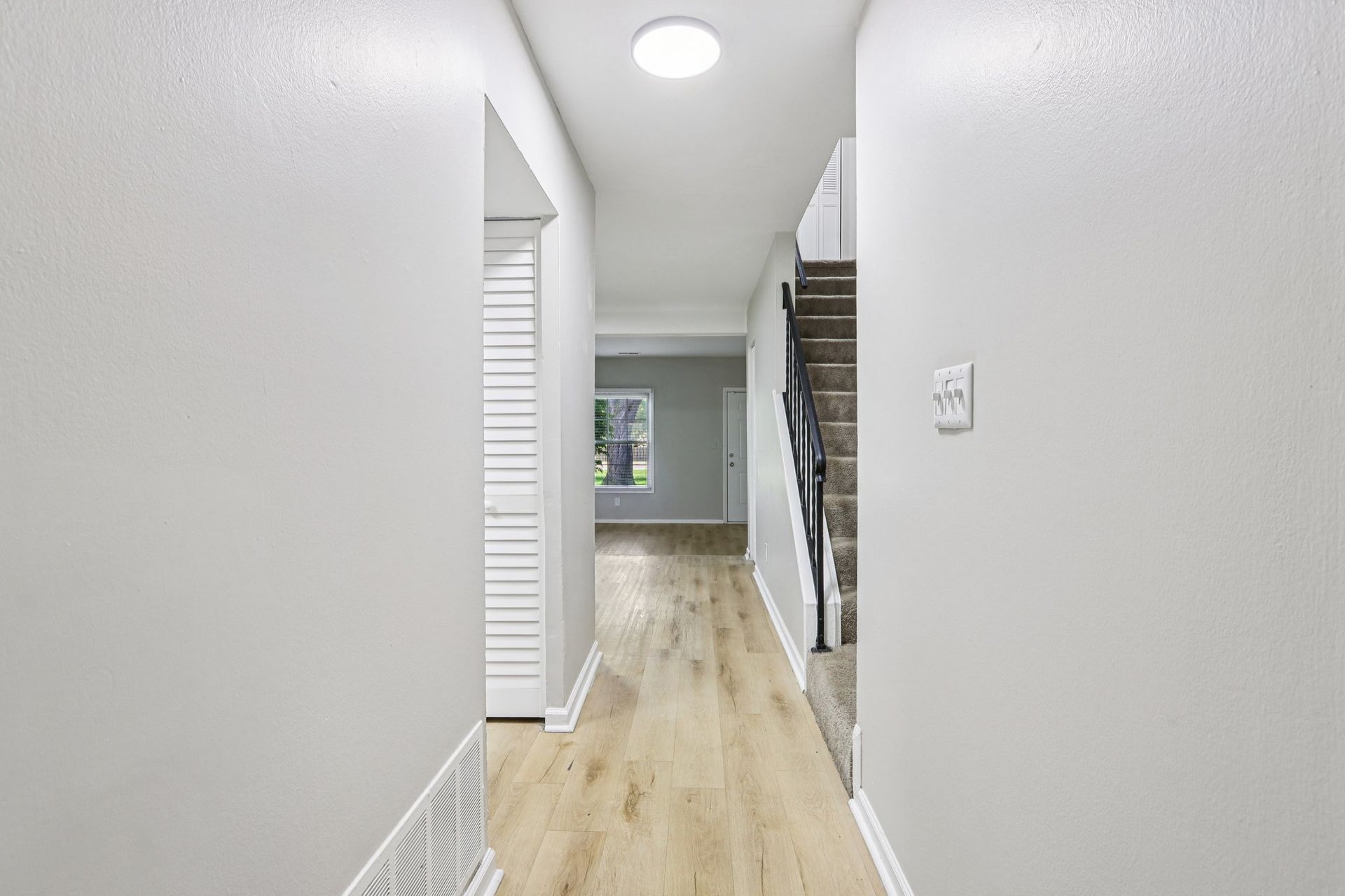Narrow hallway with light wood floors, white walls, and a staircase.