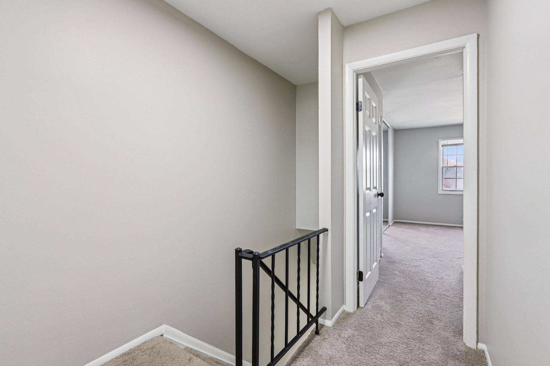 Hallway with gray walls, carpeted floor, open doorway leading to a bedroom with a window.