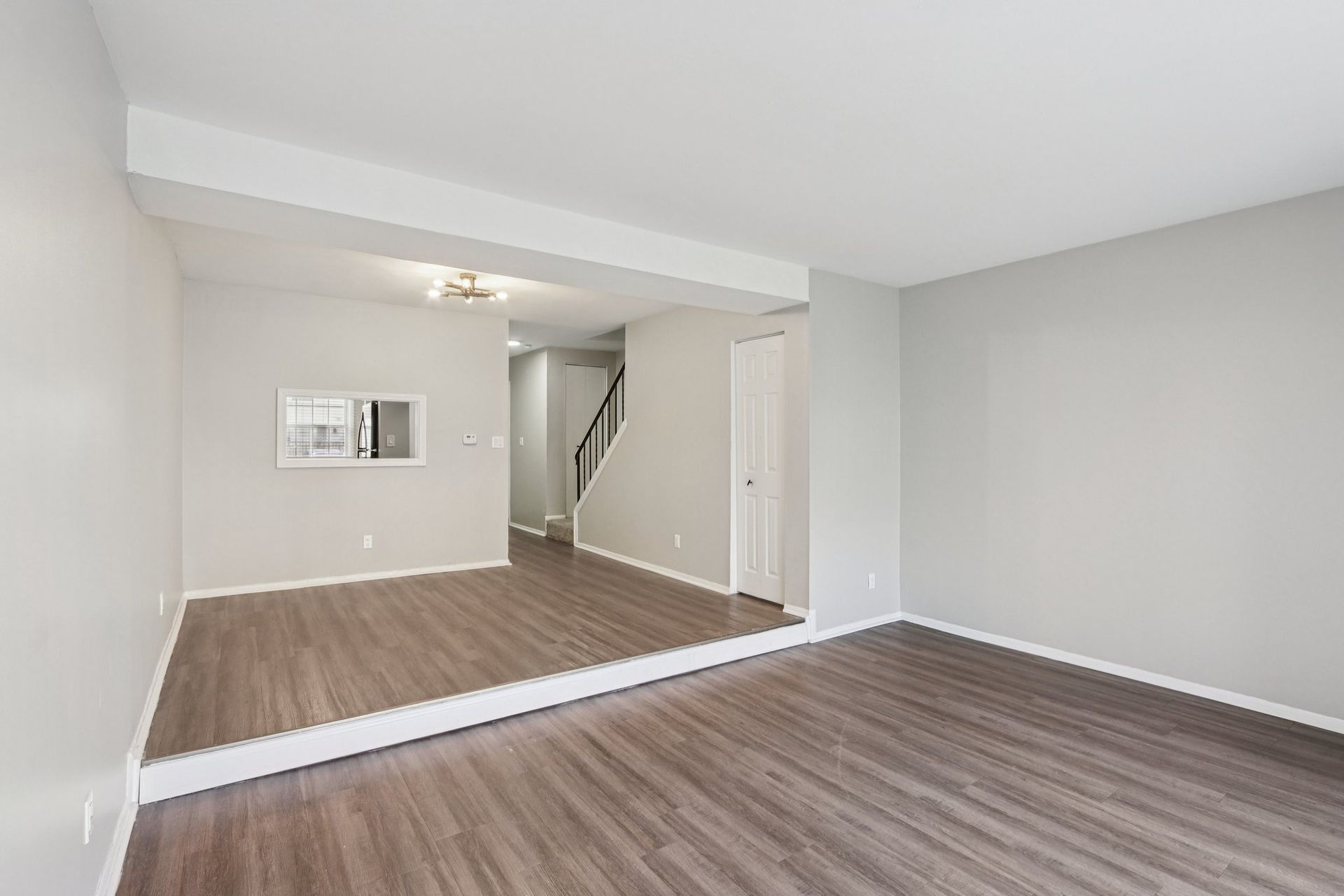 Empty living room with gray walls, wood-look floor, doorway leading to stairs.