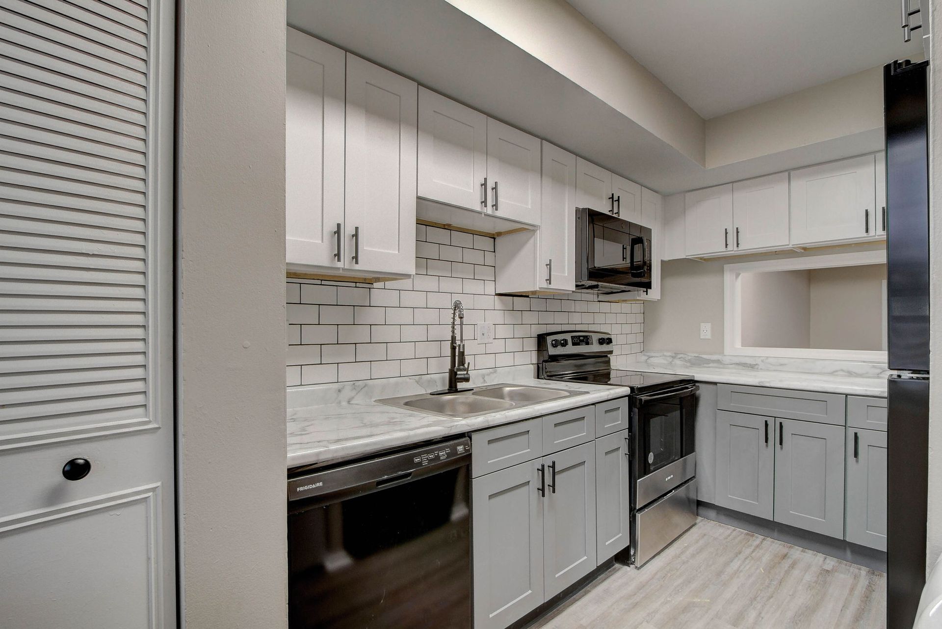 Modern kitchen with white cabinets, stainless steel appliances, subway tile backsplash, and gray flooring.