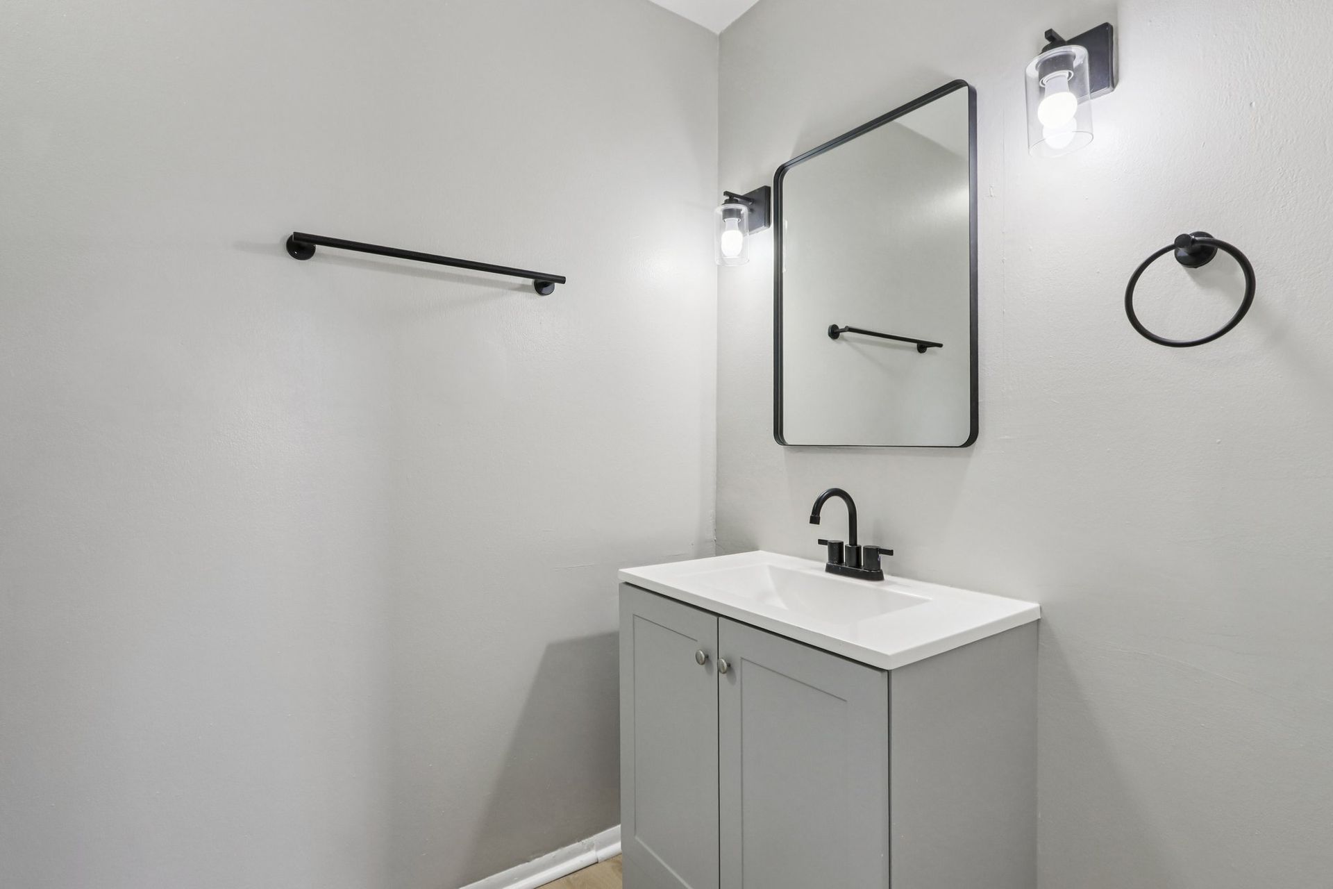 A gray bathroom with a vanity, mirror, and black fixtures.