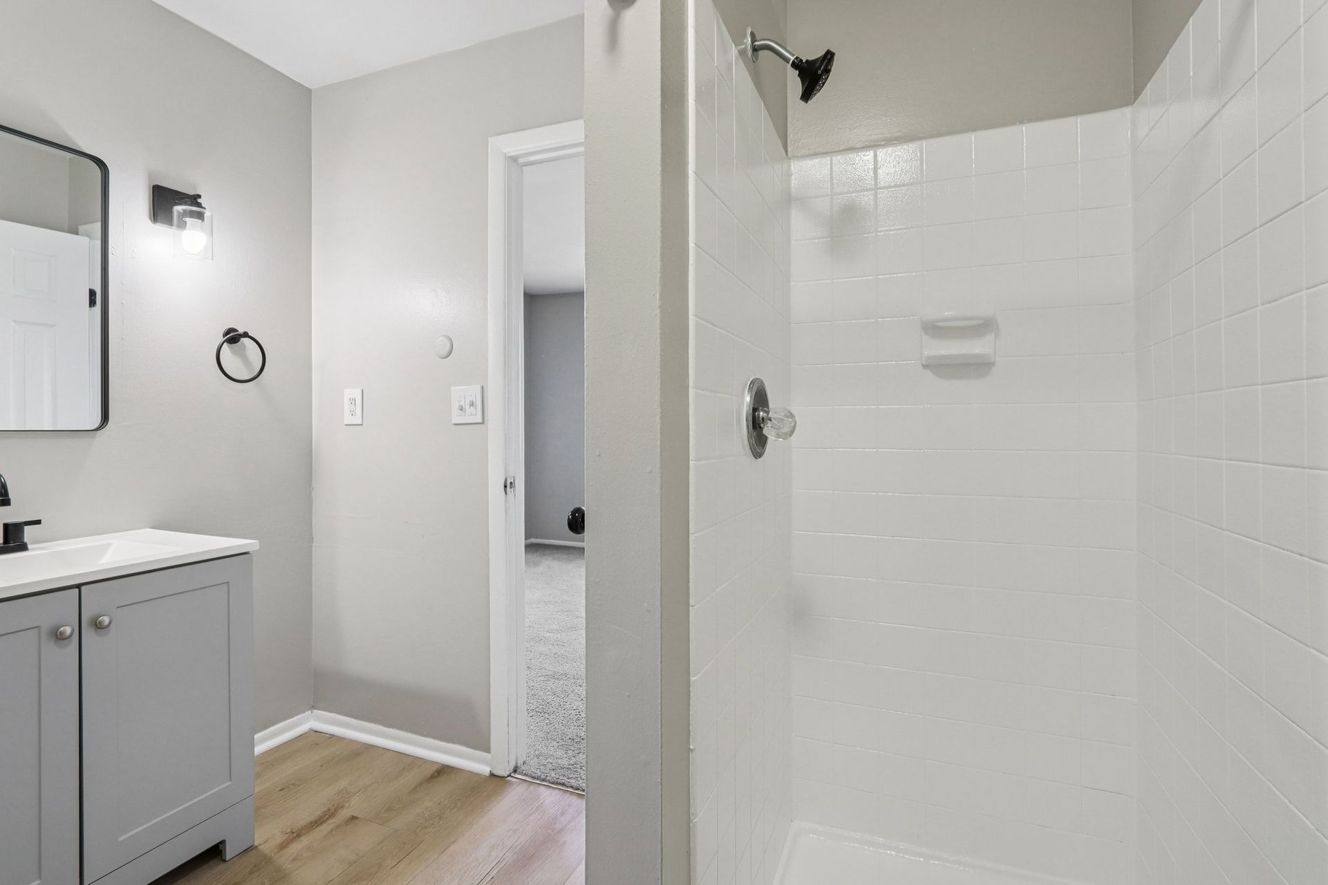Bathroom with grey walls, white shower, wooden floor, and vanity with mirror.